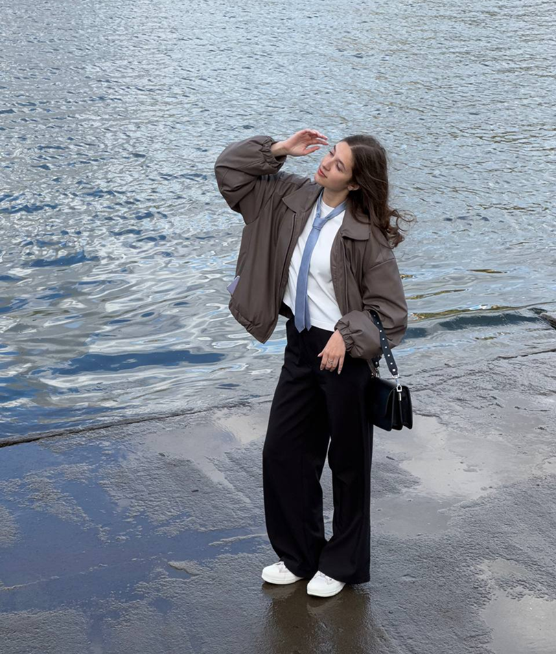 A person standing by water, shielding their eyes from the sun.